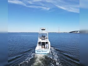 The 'Hard Money' boat is seen cruising through calm waters, with crew members actively engaged on deck — a perfect scene for fishing enthusiasts and adventure seekers.