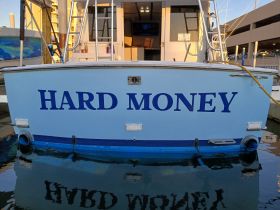 The stern of the boat named 'HARD MONEY' is prominently displayed, showcasing its unique branding while docked at the marina.