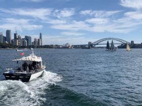 A scenic view of a boat navigating through Sydney Harbour, with the iconic Sydney Opera House and Harbour Bridge in the background, showcasing the vibrant city life and sailing activities.