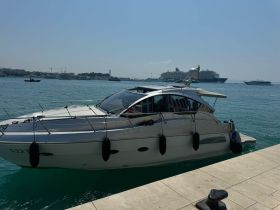 A sleek yacht docked at the harbor, showcasing its elegant design against a backdrop of distant cruise ships and clear blue waters.