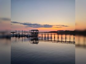 A serene sunset view over a calm waterfront, featuring a dock and boats, perfect for capturing the beauty of nature and tranquil moments by the water.