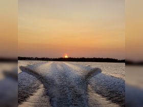 A stunning sunset view over the water, captured from the back of a boat, showcasing the serene beauty of a tranquil evening on the water.