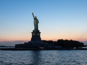 A stunning sunset view of the Statue of Liberty, beautifully illuminated against the evening sky — a must-see landmark while cruising the harbor.