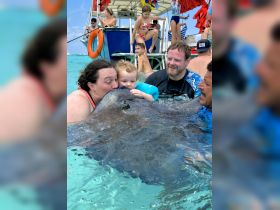 A heartwarming moment as a child interacts closely with a stingray, surrounded by family in the beautiful waters — a memorable wildlife experience in the Bahamas.