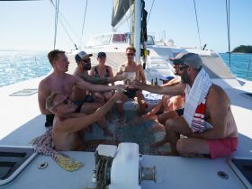 A lively group enjoys a toast aboard a catamaran, celebrating under the sun with cocktails — perfect for memorable outings on the water.