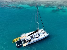 A stunning aerial view of a catamaran anchored in crystal-clear waters, showcasing its sleek design and vibrant kayaks ready for adventure.