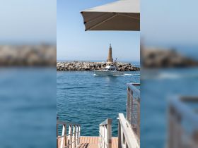 A scenic view of a boat navigating near a lighthouse, showcasing the tranquil waters and marina atmosphere.