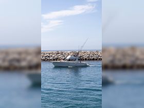 A sleek speedboat cruises through calm waters, showcasing its design and fishing gear, perfect for a day on the ocean.