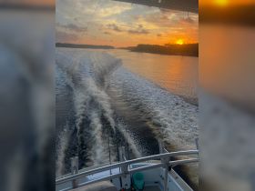 A stunning sunset view from the deck of a boat, showcasing the wake and tranquil waterway — perfect for evening fishing trips or scenic cruises.