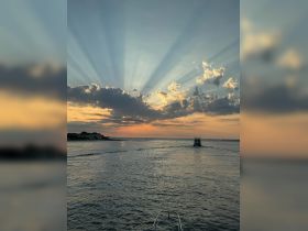 A stunning sunset over the ocean with rays of light breaking through the clouds, featuring a boat navigating the tranquil waters — a perfect scene for nature lovers and boating enthusiasts.