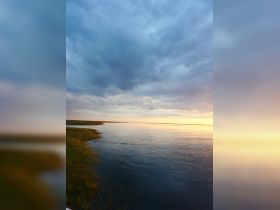 A scenic view of a calm waterway under a cloudy sky at sunset, capturing the tranquil beauty of nature.