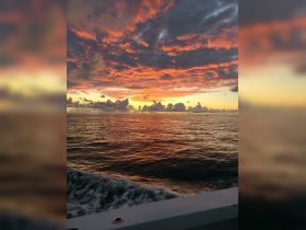A stunning sunset over the water, captured from the deck of a boat, showcasing vibrant colors and tranquil waves — perfect for evening cruises.