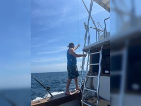 A man stands on the edge of a boat, engaged in fishing activities under a clear blue sky — a perfect moment for adventure on the water.