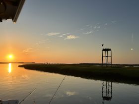 A serene sunset view over calm waters, reflecting the vibrant colors of the sky, perfect for fishing enthusiasts and nature lovers.