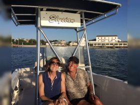 Two friends enjoy a sunny day on the boat named 'Elysian,' capturing a moment of joy and camaraderie on the water.