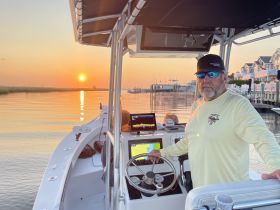 A boat captain navigates as the sun sets over the water, creating a picturesque scene perfect for evening cruises.