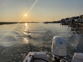 A serene sunset view from the back of a boat, showcasing the tranquil waters and reflections as the vessel moves through the calm scenery.