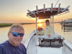 Two friends enjoy a scenic sunset aboard a boat, capturing the perfect moment on the water — ideal for fishing trips or evening cruises.