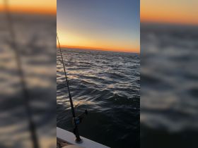 A serene sunset view over the ocean with a fishing rod in the foreground, capturing the tranquil moments of a fishing trip at dusk.