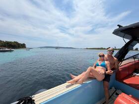 A couple enjoys a sunny day on the water, relaxing on the edge of their boat with a stunning view of the coastline — perfect for romantic getaways or summer adventures.