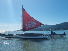A sailor navigates an outrigger boat on shimmering waters, showcasing the beauty of sailing adventures in the Whitsundays.