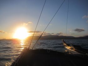 A serene sunset view from the bow of a boat, showcasing the tranquil waters and distant mountains — perfect for capturing the beauty of evening cruises.