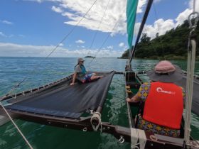 Two guests relax on a catamaran, enjoying the serene ocean views and lush island backdrop — a perfect setting for a leisurely day on the water.