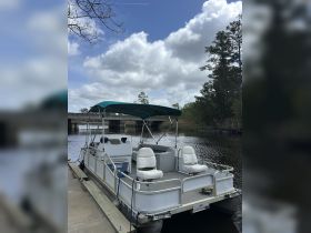 A pontoon boat docked along a serene waterway, showcasing its spacious seating and inviting design — perfect for leisurely outings on the water.