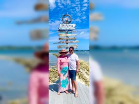 A cheerful couple poses in front of a signpost at Spanish Wells, capturing a memorable moment during their island adventure.