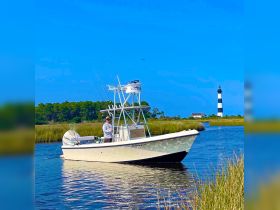 A fisherman navigates a boat through a scenic waterway, with a striking lighthouse in the background — a perfect setting for a day of fishing and exploration.