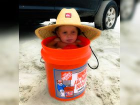 A child sits in an orange bucket on the beach, showcasing a playful and unique beach experience. Perfect for family fun in the sun.