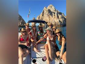 A lively group of friends enjoys a fun day on the water, celebrating with drinks and laughter against a stunning coastal backdrop.