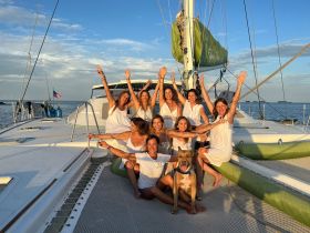 A joyful group of friends celebrates aboard a catamaran at sunset, capturing the essence of friendship and fun on the water.
