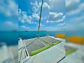 A stunning view of a catamaran's deck, showcasing its spacious netting and vibrant green cushions against a backdrop of clear blue waters and a distant island — perfect for relaxing on a sailing adventure.