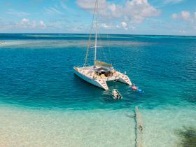 A stunning aerial view of a catamaran anchored in crystal-clear waters, with guests enjoying snorkeling and floating activities — a perfect day on the water.
