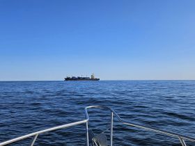 A clear view of a cargo ship navigating through calm waters, showcasing the vastness of the ocean under a bright blue sky.