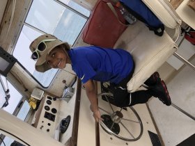 A young boy smiles while sitting at the helm of a boat, showcasing the interior cabin space and steering wheel — a perfect moment of youthful adventure on the water.