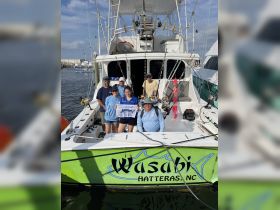 A cheerful group poses aboard the 'Wasabi' fishing boat in Hatteras, NC, celebrating their successful fishing trip — a perfect memory of adventure on the water.