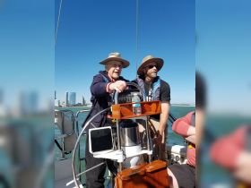 Two men enjoy sailing on a sunny day, showcasing the joy of being on the water with friends. The city skyline provides a stunning backdrop to their adventure.
