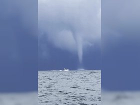 A dramatic scene captures a tornado forming over the ocean, with a boat navigating through the turbulent waters — a striking reminder of nature's power at sea.