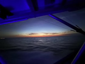 A serene view from inside a boat as it cruises through calm waters at sunset, showcasing the beautiful transition of colors in the sky.