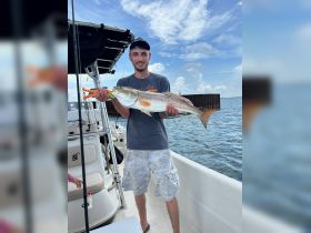 A proud angler holds up a freshly caught redfish aboard a boat, showcasing the thrill of fishing adventures on the water.