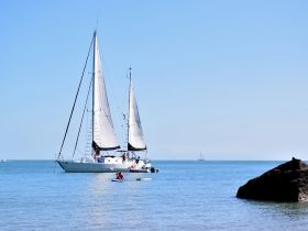 A vibrant scene featuring a sailboat and a kayaker enjoying the calm waters, perfect for adventure seekers and sailing enthusiasts.