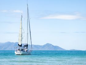 A beautiful sailboat glides through clear turquoise waters, set against a backdrop of distant mountains — an ideal scene for sailing enthusiasts and nature lovers.