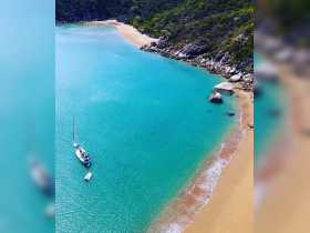 A stunning aerial view of a sailboat anchored in crystal-clear turquoise waters, surrounded by a picturesque sandy beach and lush greenery — perfect for serene getaways.