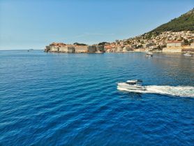 A scenic view of a boat cruising along the stunning coastline, with historic buildings and lush hills in the background, showcasing the beauty of the Mediterranean.