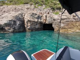 A stunning view of a rocky coastline with a cave entrance, surrounded by crystal-clear turquoise waters — perfect for exploring hidden gems while boating.
