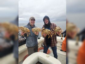 Two friends proudly display their catch of crabs while crabbing on a boat, showcasing the excitement of a successful fishing trip.