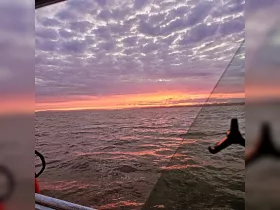 A stunning sunset over the water, viewed from a boat, showcasing vibrant colors and serene waves — perfect for evening cruises.