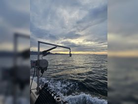 A scenic view of a boat in motion, capturing the serene waters and cloudy sky at sunset, ideal for showcasing boating adventures.